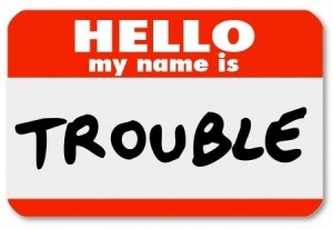 A nametag sticker with the words Hello My Name is Trouble representing a problem, issue, annoyance, mischief, danger, pain or stress