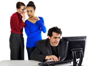Two females gossiping behind a male co-worker.